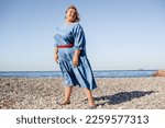 Beautiful woman plus size is walking against the background of nature in the sea. The adult woman is wearing a black maxi stylish dress. A woman of large size holds the cup pf coffee