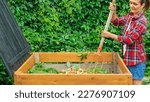 Small photo of A gardener prepares compost from food organic waste in a DIY wooden compost bin. Zero waste concept. Aging of compost for its introduction into the soil to improve its structure and fertility.