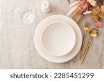 Small photo of Table setting, plate and golden cutlery on a brown background, empty wine glass, top view of the served table decorated with dry flowers