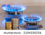 Small photo of Gas stove lit, with stacks of coins above it. Increase in gas costs and tariffs.