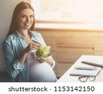 Smiling Young Pregnant Woman Eating Grape in Bowl. Young Freelancing Mother. Freelancing at Home. Pregnant Businesswoman. Healthcare Concept. Healthy Food and Lifestyle Concepts. Relaxing at Home.
