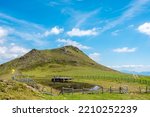 Ridge near green grassy peak of Rindernock (2024m.) and small tarn with wooden deck chairs for sunbathing, beautiful blue sky with white clouds in the background, Nock Mountains, Gurktal Alps, Austria