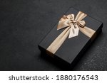 Black gift box with a golden ribbon and a large bow on a granite dark background. Place for the inscription