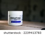 Small photo of Kyiv, Ukraine - October 16, 2022: A jar of unflavored creatine in the form of a powder from the firm Ostrovit close-up on a blurred background. Sports supplement on wooden boards