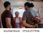 Small photo of Sons congratulate mom on the holiday. Adult brothers give a bouquet of flowers to an elderly beautiful mother. Men visiting their beloved mother on a holiday