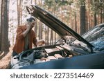A young upset man calls by phone to a car service near a broken car far outside the city. The car broke down on a trip. Calling a tow truck.