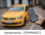 A man calls a taxi in the city through an app on his phone. Close-up. Yellow car on the background. The concept of urban transport. A guy with a phone in his hands is waiting for his taxi