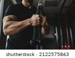 Close up on hands of unknown caucasian man at gym using rope for arms exercise muscular bodybuilder triceps training copy space dark photo
