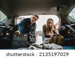 Two people couple students travel concept man and woman taking luggage baggage suitcase and other stuff and belongings from the back of car while moving into dormitory on college campus real people