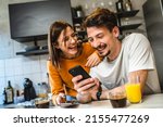 Two people young couple adult man and woman husband and wife or boyfriend with girlfriend in the kitchen in the morning with coffee juice mobile phone and digital tablet talking and chat happy smile