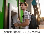 Small photo of one man young adult modern millennial tourist using atm machine to withdraw money urban life modern living concept side view male hold card copy space