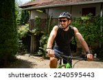 One adult caucasian man ride electric e-bike bicycle in sunny summer day getting ready in front of the house wear protective helmet and eyeglasses real people copy space