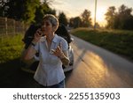 one woman mature female standing on the road in the evening sunset by the broken vehicle car automobile failed engine open hood making a phone call for help roadside assistance towing service concept