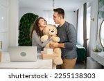 happy couple man and woman boyfriend or husband giving big teddy bear to his girlfriend or wife while having fun at home celebrating pregnancy and family relations valentine concept copy space