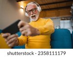 One senior old caucasian man sit at home happy smile play video games leisure activity having fun hold mobile phone smartphone have fun copy space