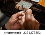 Small photo of Goldsmith jeweler man working in his crafting jewelry workshop creating and liming a white gold or silver jewel in his work studio. Jewel, craft and luxury concept.