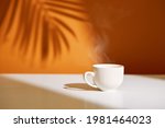 Close-up of coffee cup on table at direct sunlight. Morning coffee with steam in white cup.