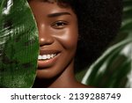 African American young woman smilling, close up potrait against green tropacal leaf. Natural skin care products concept 