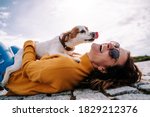 A beautiful woman laughing while her pet is licking her face in a sunny day in the park in Madrid. The dog is on its owner between her hands. Family dog outdoor lifestyle