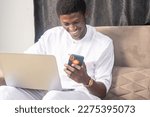 Small photo of overexcited handsome businessman seated working on laptop and using mobile phone