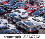 Sale of new and used cars in a dealership. Lots of cars in the car park. Black, white, silver and red cars of unknown brands