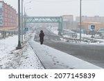 Snowy weather in the city. A woman walks along the snow-covered sidewalk. Snowfall on the street of a northern city in the Arctic. Cold weather in May in the far north of Russia. Anadyr, Chukotka.