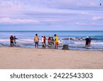 Small photo of Cartagena, Bolivar Colombia - 1 February 2024: fishermen finishing winding the ropes with which they drag the trammel net with the fish collected on the beaches of Cartagena de Indias, Colombia: