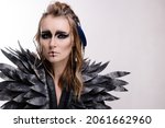 Small photo of Beautiful woman in makeup and costume for halloween on a white background. Fantasy image of a harpy or valkyrie. Celtic mythology character. Wings and feathers. Smokey eyes. Carnival girl black bird