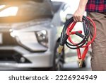 
Close-up of mechanic holding car battery jumper cable when experiencing dead battery in garage battery extension cable car maintenance service concept