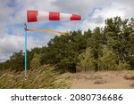 Small photo of Windsock on a sandy beach in strong wind, Red and white fabric cone designed to indicate the direction and approximate wind speed, coastline, dense green forest