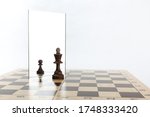 Small photo of the king is reflected in the mirror as a pawn on white background. underestimation of their abilities