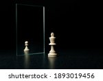 Small photo of the king is reflected in the mirror as a pawn on white background. underestimation of their abilities