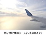 Small photo of Airplane wing flying above white clouds obscure light from the sun. View from aircraft window.
