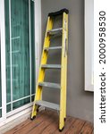 Small photo of Fiberglass fireproof ladder, yellow and black color, 6 feets, leaning against house wall, vertical image