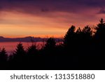 Trees silhouettes against a beautifully colored sky at dusk, with mountains layers in the background