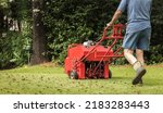 Small photo of Man using gas powered aerating machine to aerate residential grass yard. Groundskeeper using lawn aeration equipment for turf maintenance.