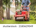 Small photo of Man using gas powered aerating machine to aerate residential grass yard. Groundskeeper using turf aeration equipment for lawn maintenance.