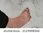 Small photo of Senior walks barefoot on the snow. Bare sinewy male legs. Tempering exercises.