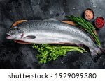 Small photo of Uncooked raw sea salmon whole fish on a wooden board with herbs. Black background. Top view.