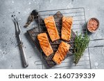 Grilled salmon fillets steaks with salt pepper and herb on grill. Gray background. Top view.