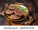 Grilled burger beef meat patty with herbs and spices on steel plate. Wooden background. Top view.