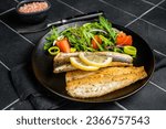 Roasted sea bass fillet with salad, Branzino fish. Black background. Top view.