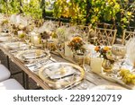 Wedding decorations. Served wedding table with golden plates, napkins, decorative fresh and dried flowers, candles and and light bulbs. Celebration details, wedding outdoor	
