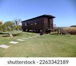 Small photo of Punta del Este, Uruguay - Feb 22, 2015: Boxcar turned into office. Old wooden railway carriage. Green lawn, concrete pathway, beautiful blue sky without clouds. Hot summer day. Work from home concept.