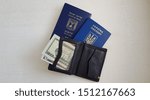 Small photo of black wallet with USA dollar bills lay open on two passports of Ukraine and Israel on white table