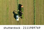 Small photo of Aerial view of a combine harvester and tractor with trailer in sunny weather. The combine harvester collects freshly cut grass.