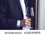 Horizontal close up of Caucasian man in black suit and white shirt holding a tall glass with rose wine  at an event by the window natural lighting