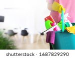 Small photo of Charwoman standing with a bucket and cleaning products on blurred office background.