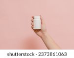 Plastic bottle (tube) in hand on a pink background. Packaging for vitamins, tablets or capsule, or supplement