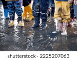Small photo of Children's feet in rubber boots, raining pants, North Sea mudflat hike at low tide, close up.